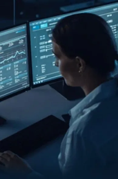 a professionally dressed woman sits in front of multiple computer monitors examining the data present
