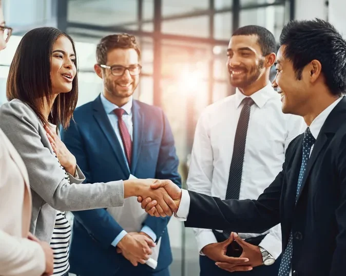 a group of five professionally dressed people stand in a circle, while two shake hands